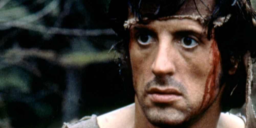 Un John Rambo ensangrentado (interpretado por Sylvester Stallone) mira fuera de la pantalla con una expresión en blanco en su rostro en First Blood.