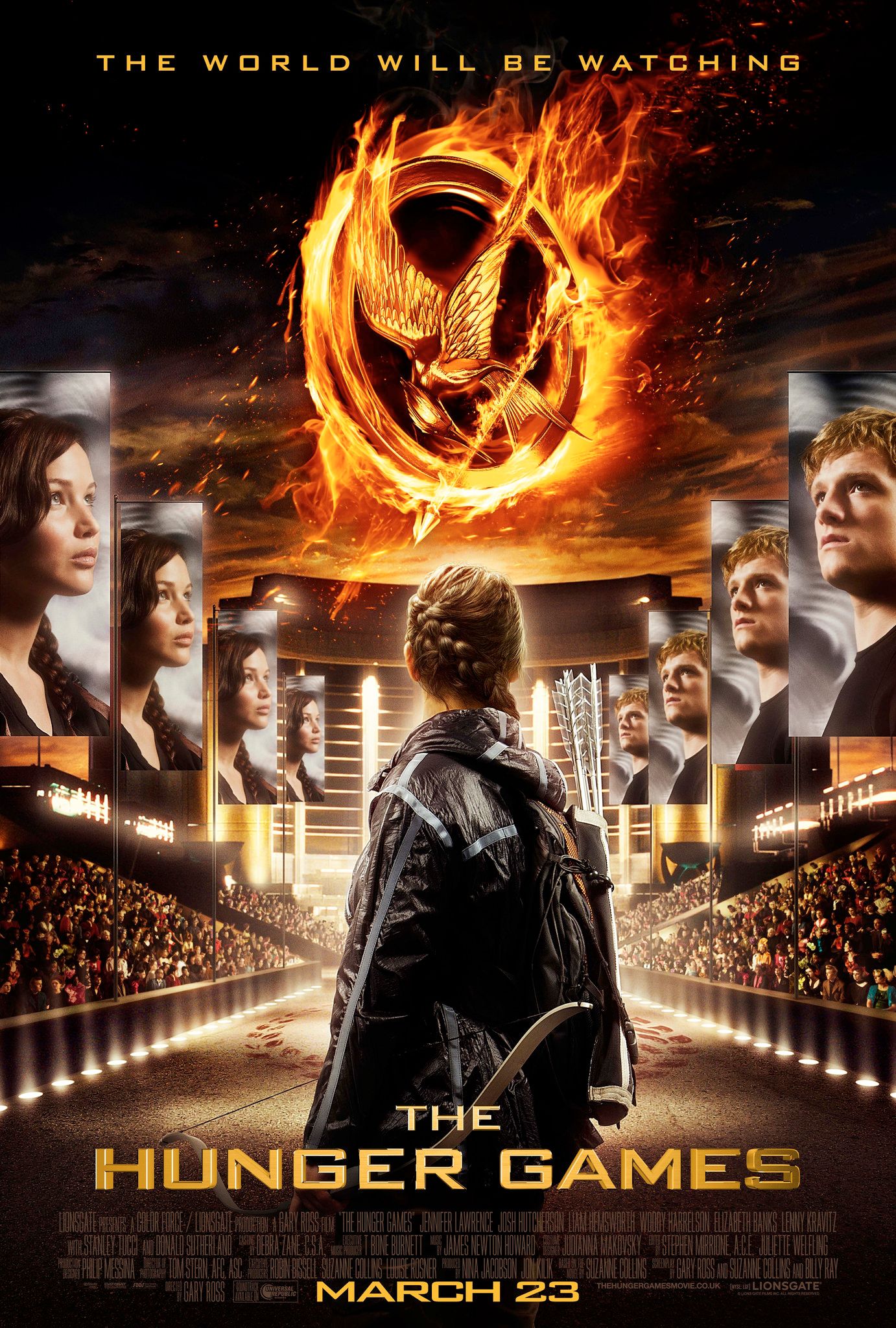 Katniss se para frente a carteles de ella y Peeta con el símbolo del Sinsajo en llamas en el centro en el cartel de la primera película de Los Juegos del Hambre.