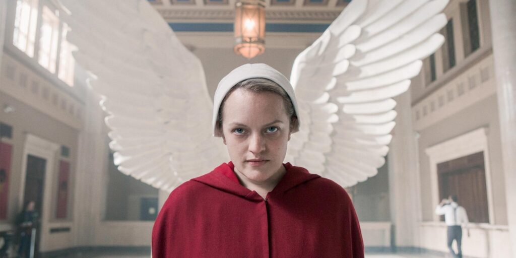 La Doncella Escarlata de Junio ​​mira hacia la cámara con alas de ángel detrás de ella.