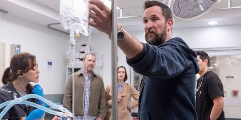 Dr. Robby adjusts an IV bag in an operating room while the patient's parents are looking at the TV Pitt show
